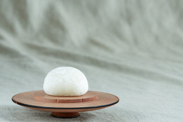 Closeup on a bright white daifuku mochi on a wooden plate on a khaki green fabric.