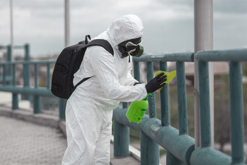 Quarantine, coronavirus infection. A man in protective equipment disinfects with a sprayer in the city. Cleaning and Disinfection at the street. Protective suit and mask. Epidemic.
