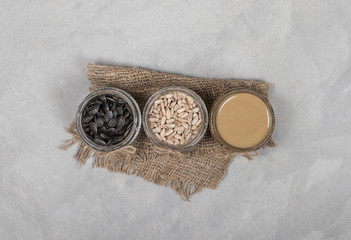 Sunflower seed paste, sunflower seeds peeled, sunflower seeds in husks in jars on a linen napkin in rustic style on a light gray background top view