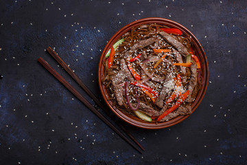 Wok beef soba noodles with pepper souce in a brown bowl on a black surface.