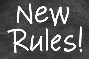 Text NEW RULES written on black chalkboard