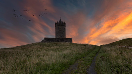 Fototapeta na wymiar Doonagore castle at sunset, Co. Clare, Ireland Epic sunset landscape the wild atlantic way in Doolin County Clare, Ireland. Beautiful scenery sky cliouds landscape with an old Irish Castle and coastal