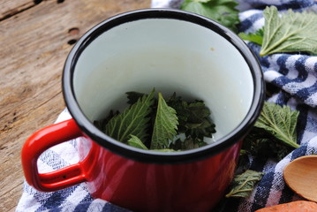 Fresh Nettle Leaves in a Red Enamel Mug, ready for Nettle soup. Wooden background.