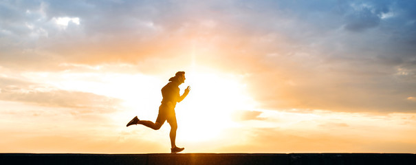 Silhouette of a running young man in sportswear at sunset. Sport lifestyle