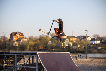 Teenager jumping on a scooter. Leap at sunset. Skate park.