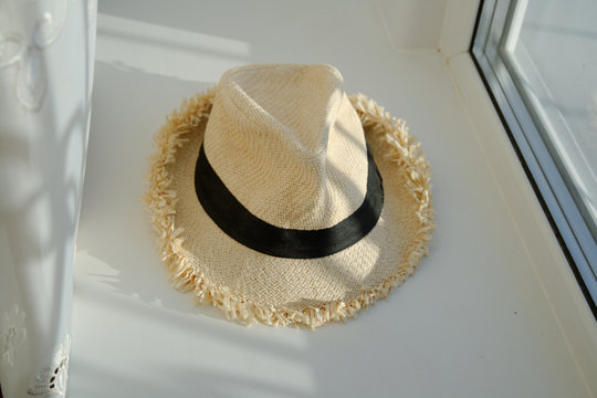 a white summer hat with a black ribbon lies on a white windowsill.