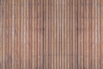 A solid wall of aged brown wooden planks with clogged nails located vertically. Concept for texture, background, interior.
