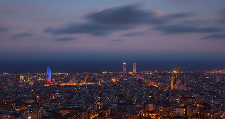 Illuminated skyline with cathedral Sagrada Familia and tower Torre Agbar in Barcelona during night, street lights from Bunkers del Carmel.
