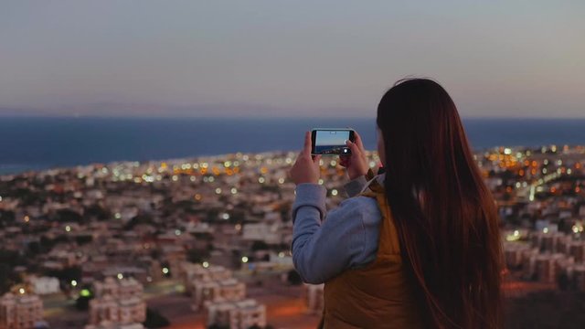 Woman take picture of the sea by smartphone in the evening. Woman stay on top of the mountain and looking Into Horizon, slow motion, full hd