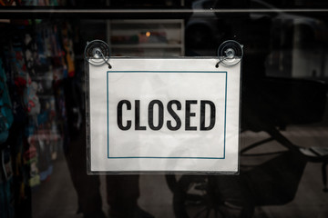A printed paper with the words closed in bold and border hangs in a storefront or business glass window during the COVID-19 outbreak pandemic and stay at home orders effecting business and the economy