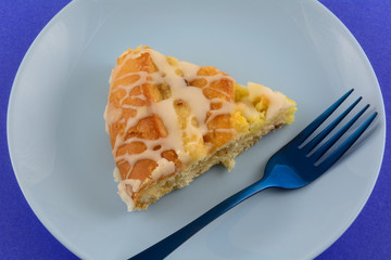 Closeup of slice of apple pecan danish on plate on blue plate with blue fork on blue background
