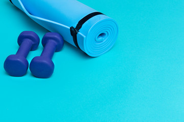 Two dumbbells of blue color  and gym mat on blue background. Healthy lifestyle concept.