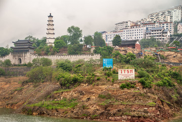 Baidicheng, China - May 7, 2010: Qutang Gorge on Yangtze River. Gate with tower to Historic fortress with pagoda, and highrise residential housing under White mist over hills Ship signs add color. 