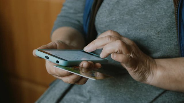 hands of an old woman in an online bank using a smartphone, online shopping with a credit card, home lifestyle