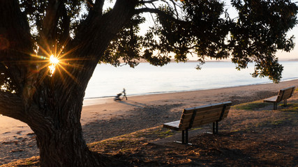 Early morning sunrise at Milford Beach in Auckland. Woman pushing baby stroller with intentional...
