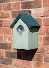 Simple and minimal green painted wooden bird box shot at an angle affixed to a red brick wall.