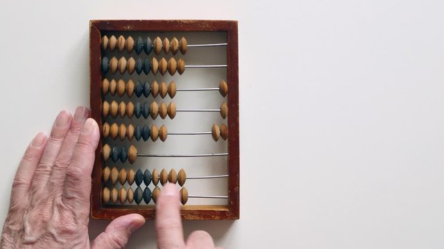 A Elderly Man Moves Wooden Knuckles On A Outdated Vintage Wooden Abacus On A White Desk.