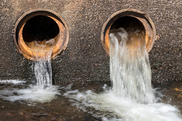 Water flowing from pipes under causeway on road