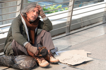 Homeless man is sitting down on walkway in town. He is very sadly and unhappy.poverty,despair,Photo Sympathetic and hope concept.