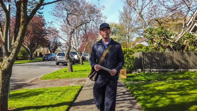 Postal worker hand delivering mail while walking down a sidewalk in an upscale neighborhood