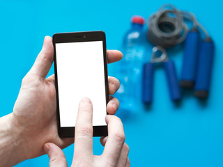 The man touches empty white smartphone screen against the background of sports equipment.