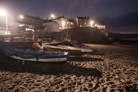 Boats pulled up on sand for night with surrounding street lights illuminating the buildings and beach.