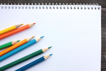 Open drawing album and colored pencils on old wooden background. Top view. Copy space	
