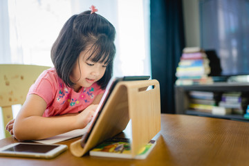 Fototapeta na wymiar Online education, Online learning.Little asian girl studying homework math during her online lesson at home with tablet, Social distance, Quarantine, self isolation, Online education concept.Covid-19.