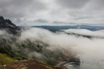 View of fog coming ashore over tree laden hills along the Oregon coast