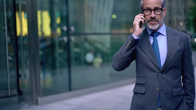 Male entrepreneur consulting with colleague about ideas for investing talking via smartphone application during strolling, business man making international conversation with partner
