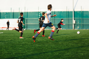 Obraz premium Boys in white black sportswear running on soccer field. Young footballers dribble and kick football ball in game. Training, active lifestyle, sport, children activity concept