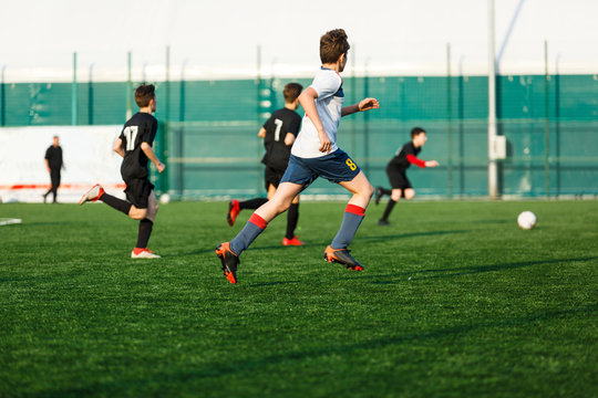 Boys in  white black sportswear running on soccer field. Young footballers dribble and kick football ball in game. Training, active lifestyle, sport, children activity concept