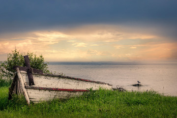 old abandoned row boat sitting beside lake under a setting sun