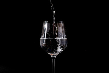 Pouring water into a clear glass. Isolated on a black background. 