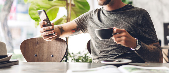 Handsome hipster man relaxing using digital smartphone with coffee and looking at screen typing message at table in cafe and restaurant,playing game online and social media