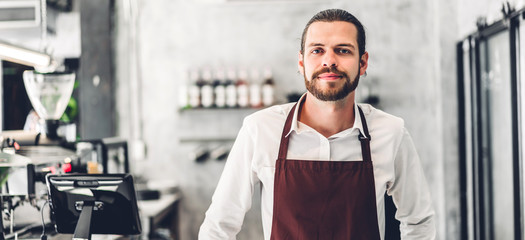 Portrait of handsome bearded barista man small business owner smiling behind the counter bar in a...