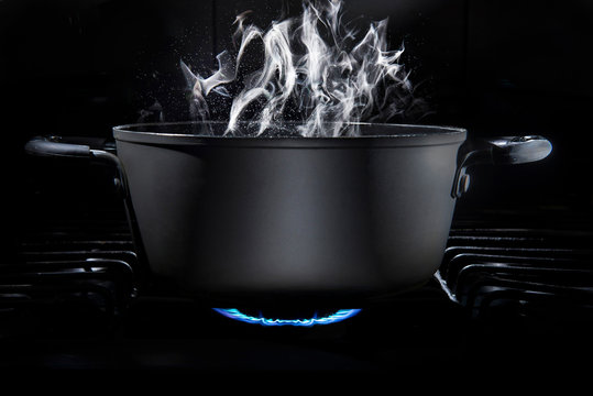 Cooking Pot On Stove Fire With Food Inside In A Dark Kitchen And A Black Background With Steam Coming Out Of The Cooking Pot, Low Key Light, And Dark Food. Cooking At Home Or Culinary School Concept. 