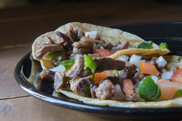 Mexican carne asada tacos or grilled beef tacos with salsa Bandera or pico de gallo on a black plate in a vintage wooden table, taquitos as part of Latin Mexican gastronomy.