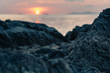 Sun setting in the sea over rocks on the beac in summer