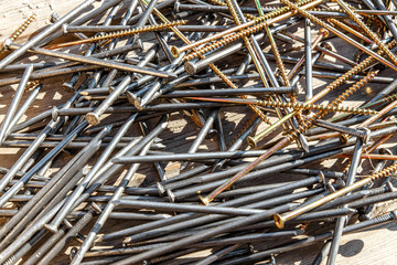 Iron nails and screws on a wooden background. Long, metal, carpenter's nails and self-tapping screws for construction. Fixing tool. The view from the top.