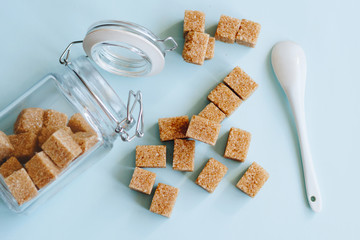 Brown cane refined sugar in a jar and white spoon on light blue background.
