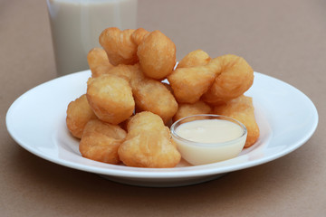 Chinese doughnut stick with Sweetened condensed milk in the small glass cup on the white round dish with a glass of milk on brown floor.