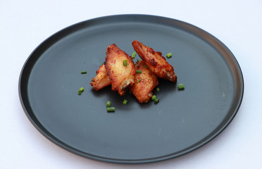 Grilled chicken wings in the black round plate on white floor. Sprinkled with spring onions.