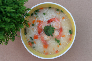 Rice congee mixed with shrimp in the round bowl on the brown floor. Sprinkled with spring onions and coriander.