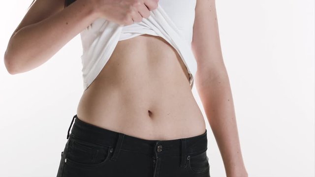Medium shot of a girl's fit and slim belly as she lifts her shirt to show her bare stomach.

