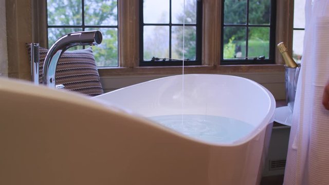 A woman prepares a romantic bath for two with essential oils and champagne.