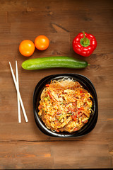 Black plate with funchose and chicken with vegetable filling on a wooden table and fresh vegetables.