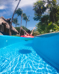 Happy young girl with bikini in red float at beautiful "pool path" with buildings with straw roof, plants palms, and blue sky, Mexico