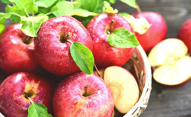 A lot of fresh Royal Red Gala apples with green leaf and water drop in basket on wooden background.