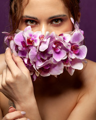 Portrait of a girl with bright makeup in a mask of orchid flowers on her face. Protective mask of flowers. Beauty protection. Flower mask. Natural protection. Close-up portrait.